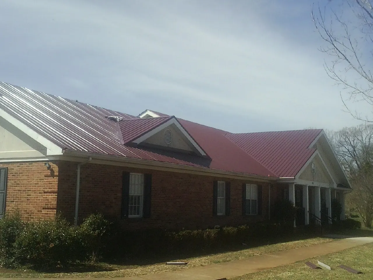 Red metal roof with gabled entries on a long brick building, from a Hail Damage Roof Repair job in Barney