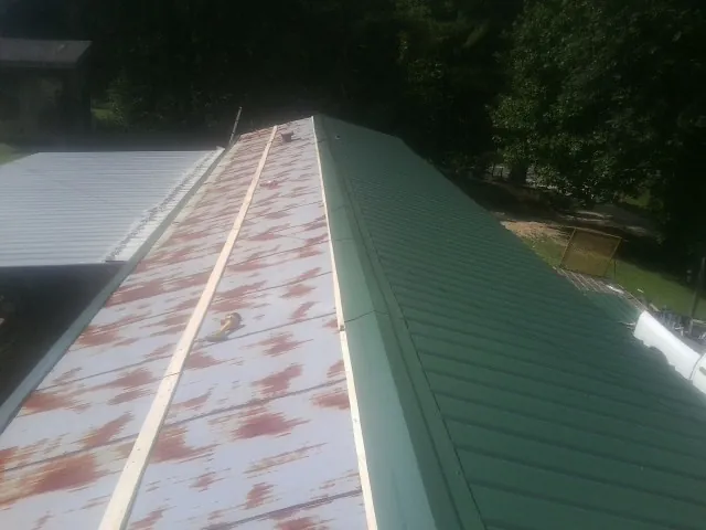 Old rusted panels beside newly installed green metal roofing — Wind Damage Roof Repair by Roofing Brothers in Barney