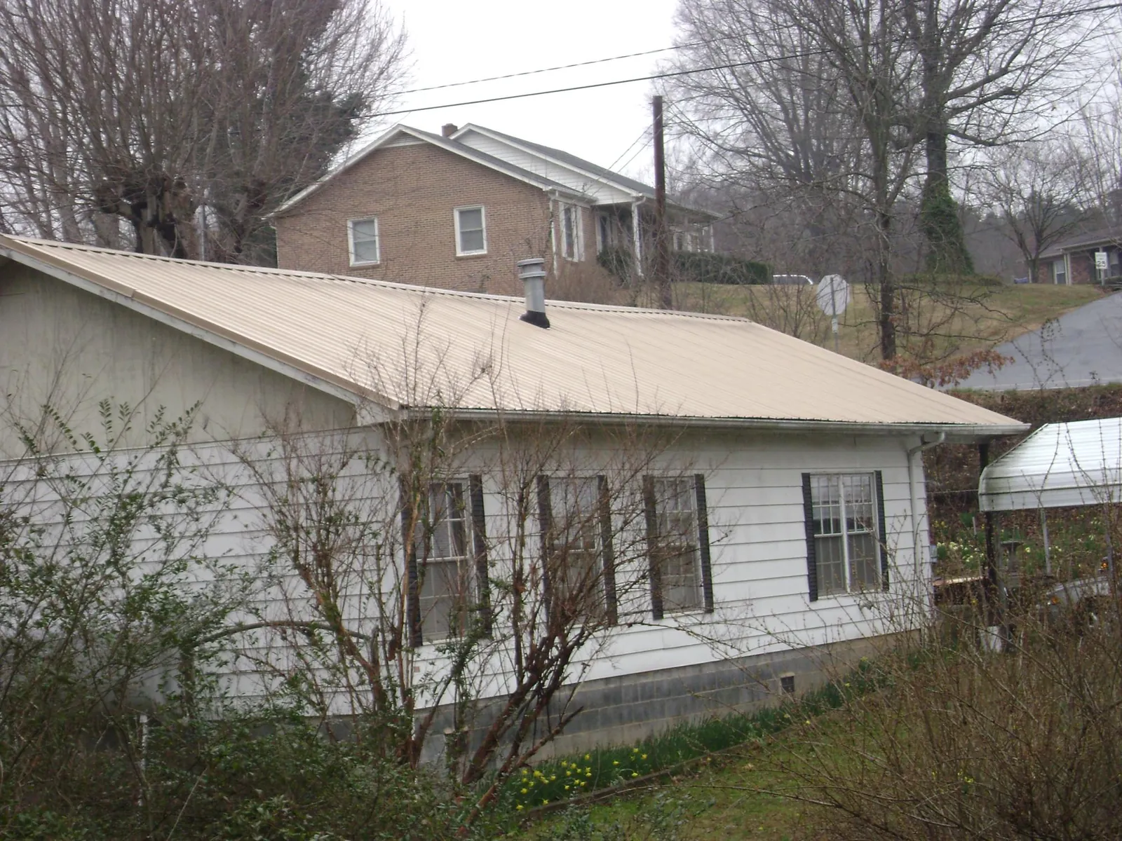 Tan metal roof on a white sided house set into a hillside — Commercial Roofing by Roofing Brothers in Barney